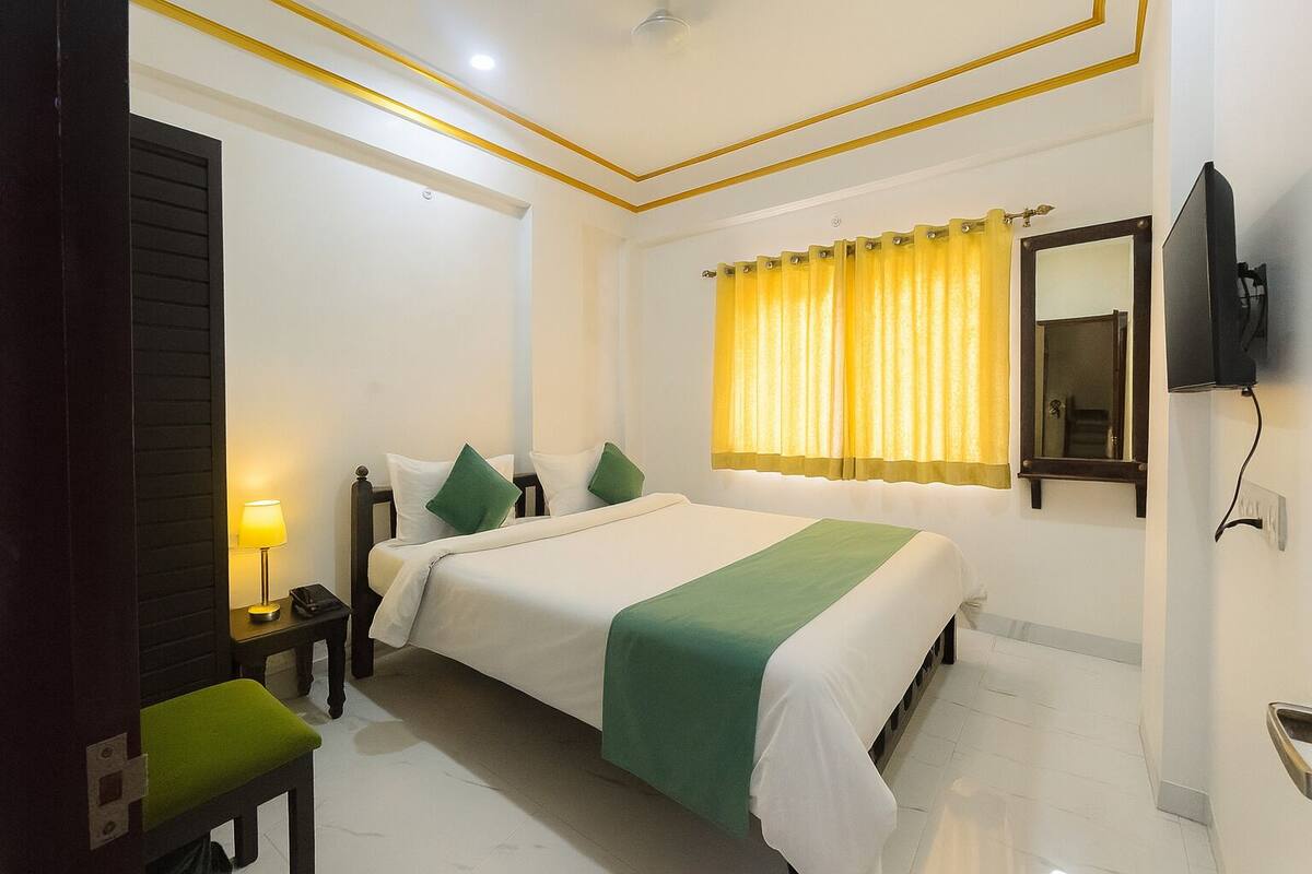 A hotel room with a bed, bedside tables, a lamp, a mirror, and a television.