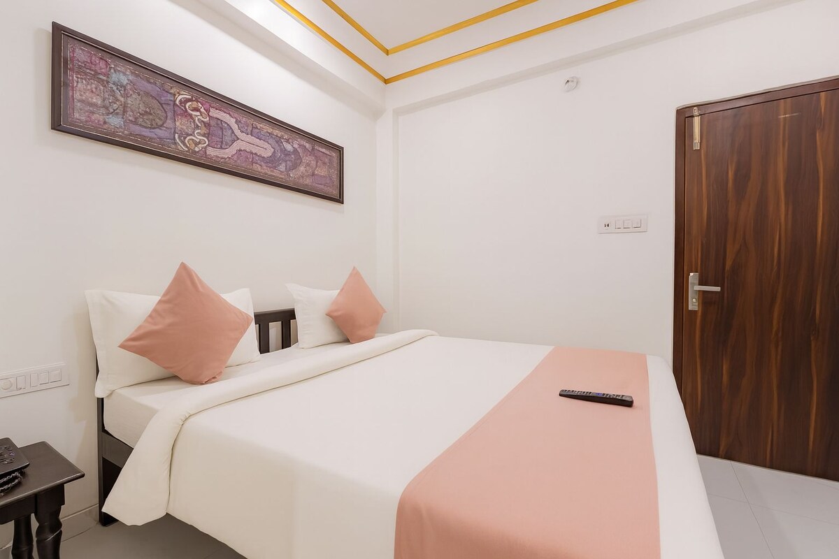 Een slaapkamer met een bed, een nachtkastje, een afstandsbediening, een deur en een kunstwerk aan de muur.