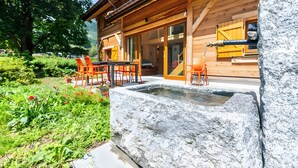 Una cabaña de madera con fuente de piedra, asientos exteriores y un jardín.