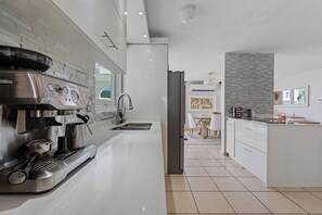 A modern kitchen with a built-in espresso machine, a sink, and a dining area with a table and chairs. - Casa Palma Serena - Garden Retreat • Tropical Stay (Santa Isabel)