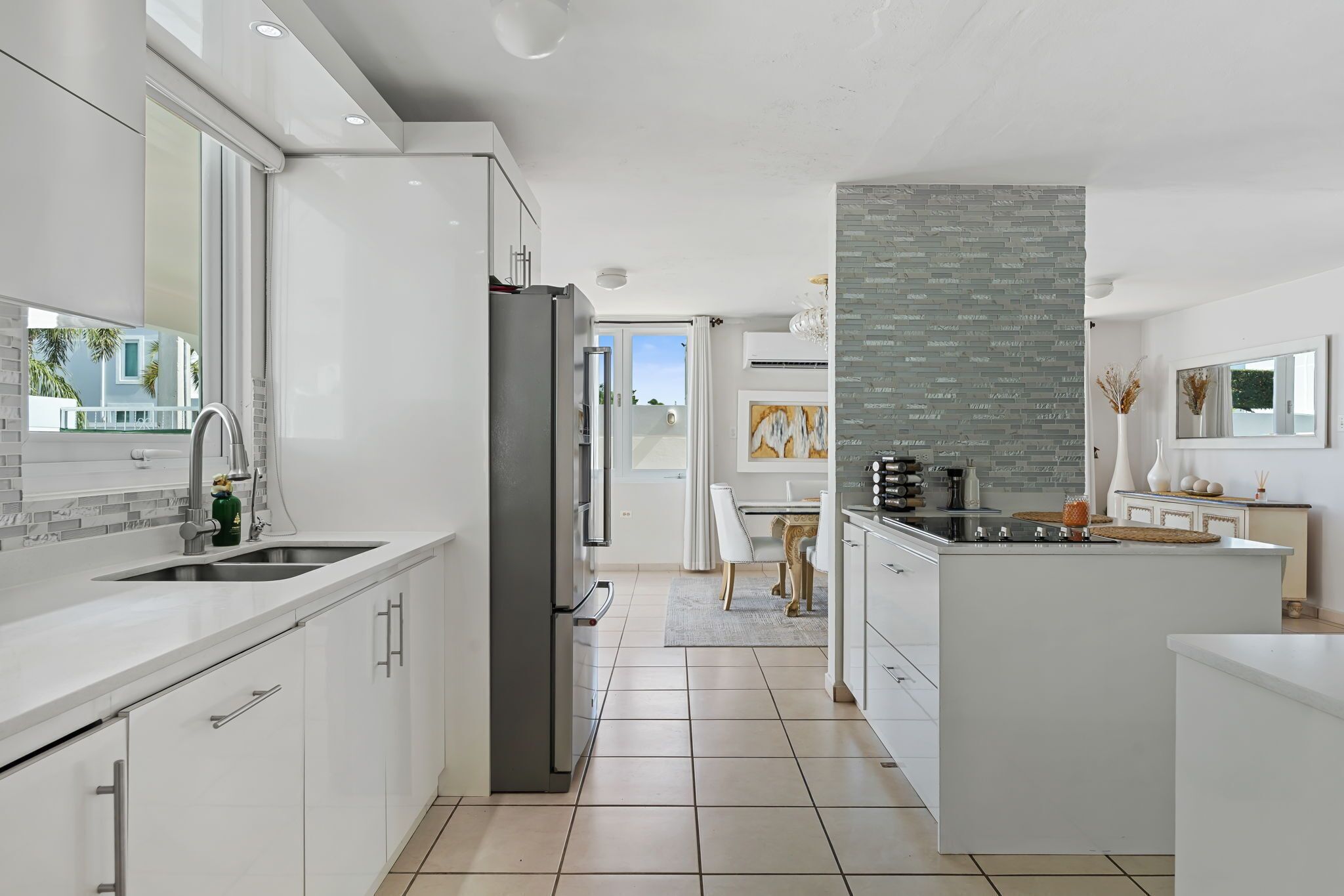 A modern kitchen with white cabinetry, a stainless steel refrigerator, and a central island with a stove.