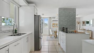 A modern kitchen with white cabinetry, a stainless steel refrigerator, and a central island with a stove.