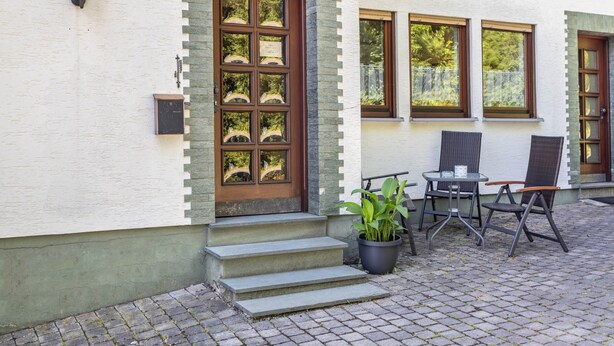 Ein Gebäude mit einer großen Holztür, einer kleinen Außenbereich-Sitzgelegenheit mit zwei Stühlen und einem Tisch sowie einem Blumentopf.