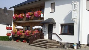 Ein zweistöckiges Gebäude mit einem Blumen geschmückten Balkon, einem Schild das ein Restaurant anzeigt und einer Treppe, die zum Eingang führt.