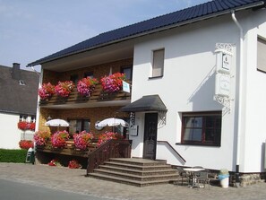 A two-story building with a balcony adorned with flowers, a sign indicating a restaurant, and a staircase leading to the entrance. - Lisa Apartment in the Nature Village of Dreislar (Medebach-Dreislar)