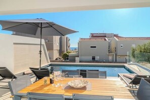 Ett utomhusområde med en pool, ett träbord, stolar och ett parasoll.