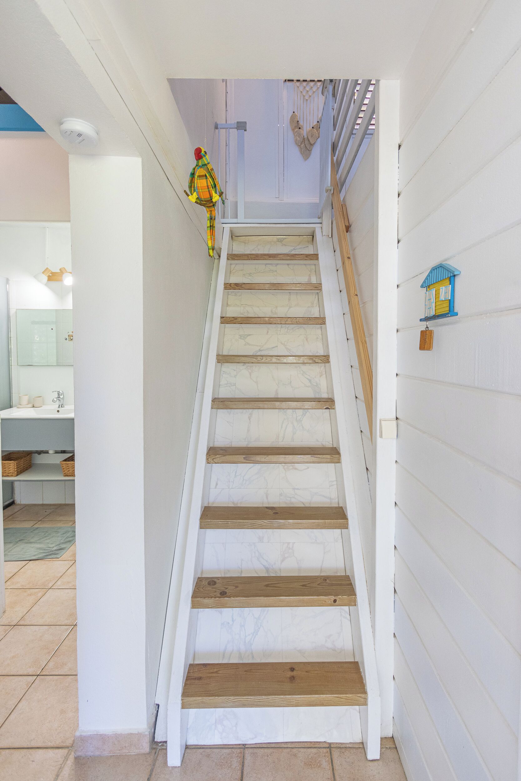 Un escalier avec des marches en bois et des murs blancs, menant à une pièce décorée avec une petite maison bleue.