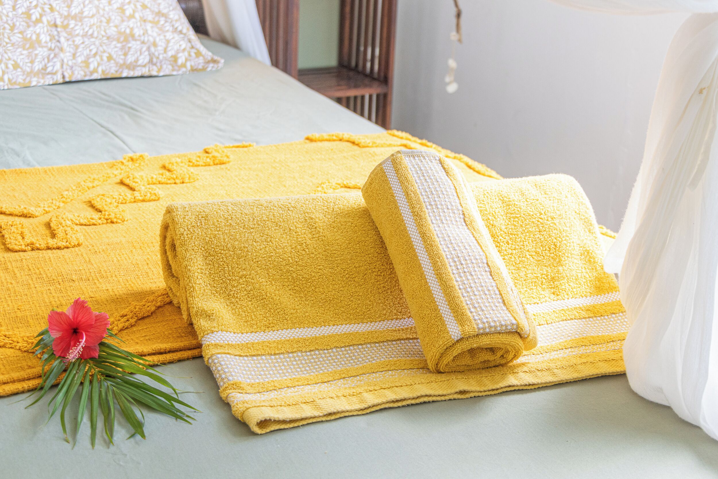 A neatly made bed with a yellow towel and a rolled-up towel with a striped pattern.
