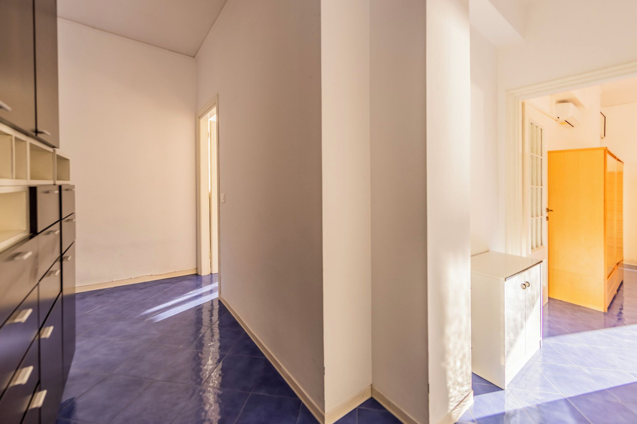 A hallway with a blue-tiled floor, a white door, and a small white cabinet.