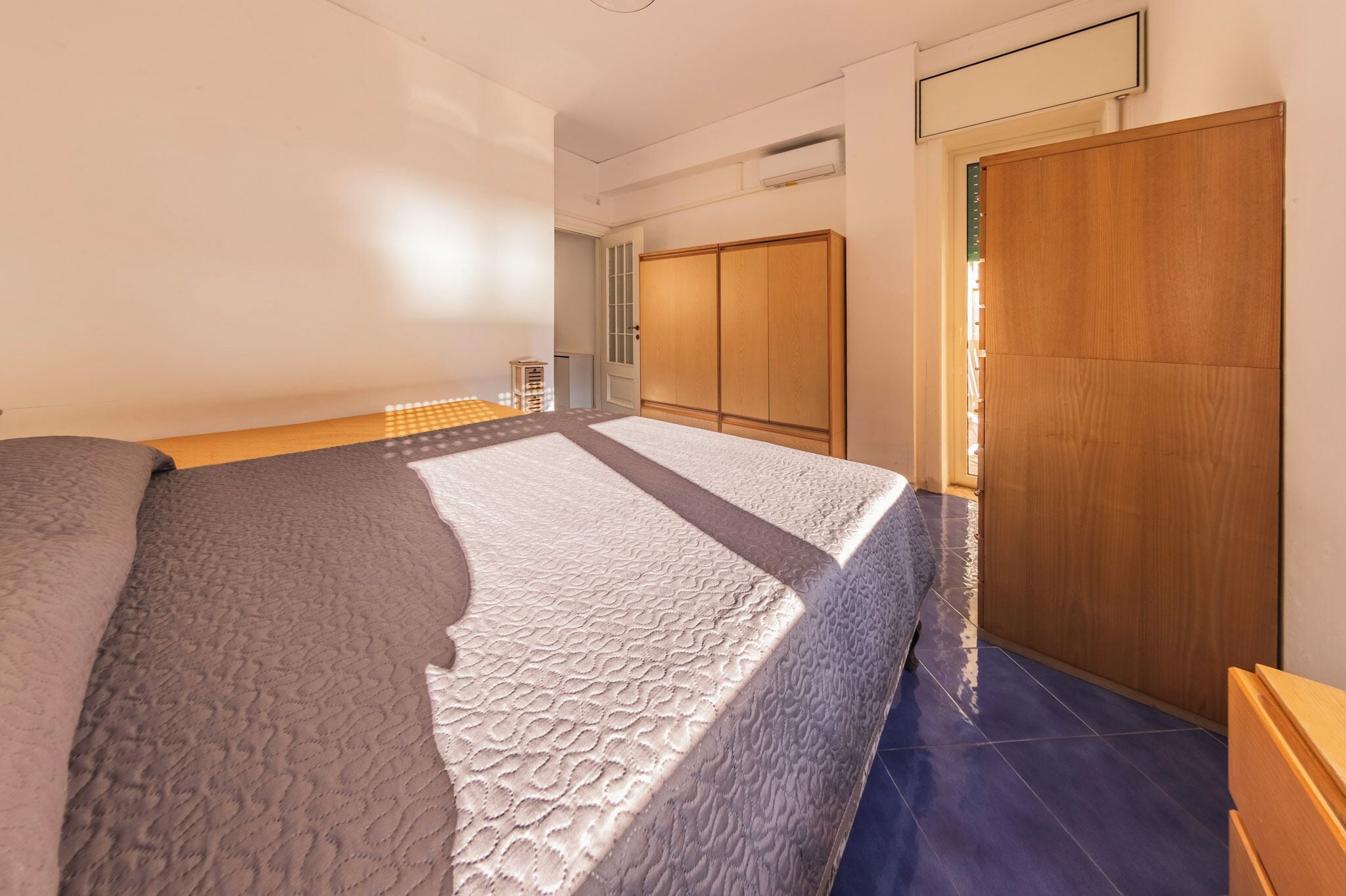 A bedroom with a bed, a wooden wardrobe, and a blue-tiled floor.