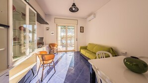 A room with a glass door leading to a balcony, a green sofa, a white table, and a wicker chair. - Casa D'Amato - Maiori (Maiori)