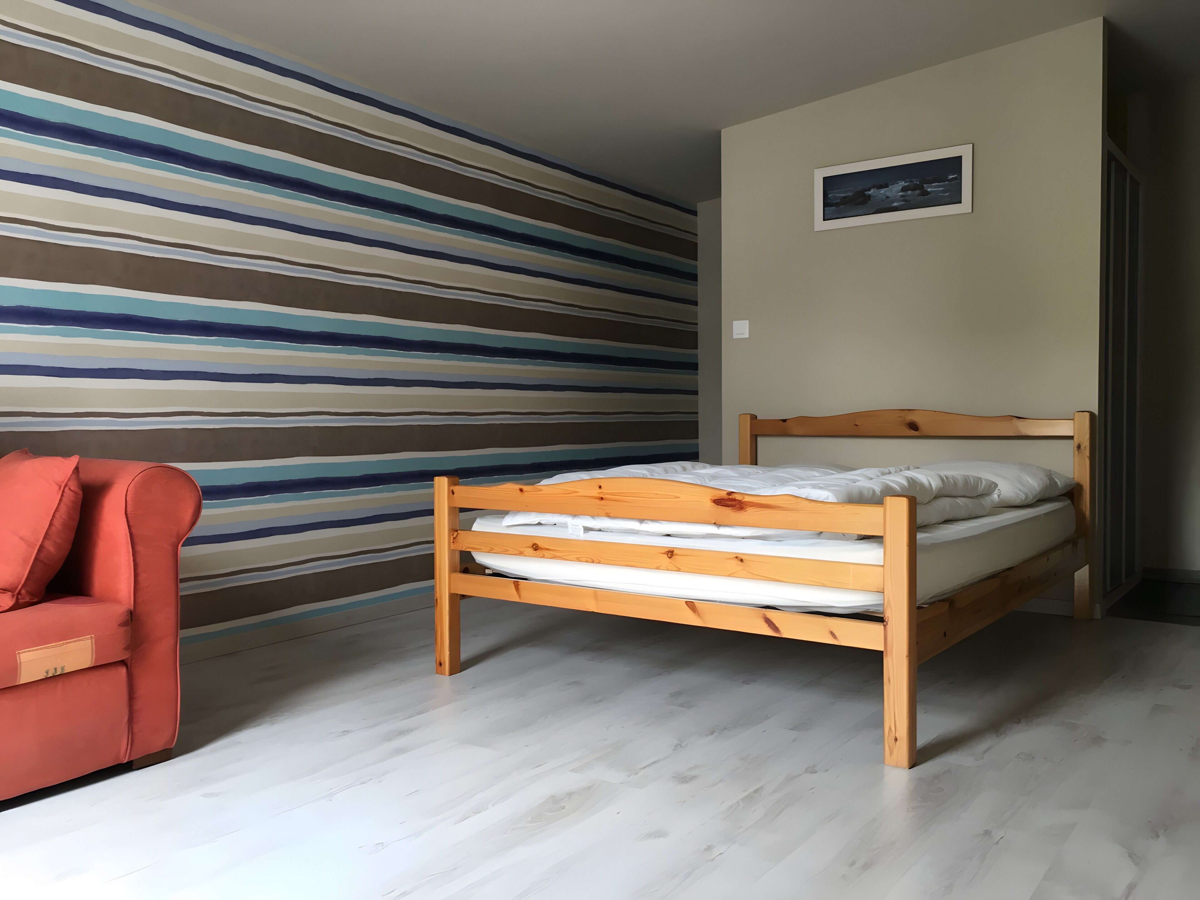 Ein Schlafzimmer mit einem hölzernen Bett, einem roten Stuhl und einer gestreiften Wand.