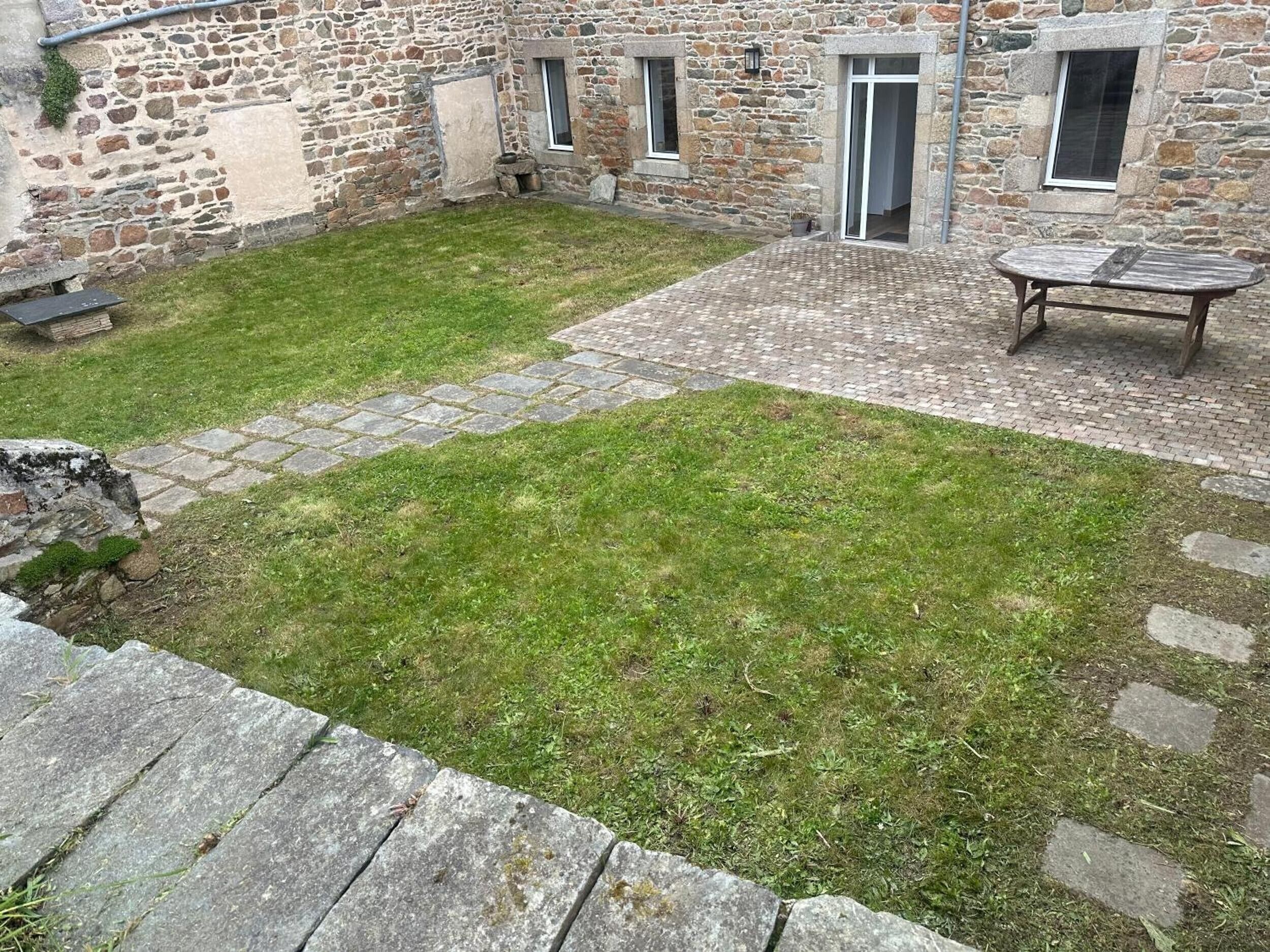 A stone building with a grassy courtyard, a paved patio, and a table.