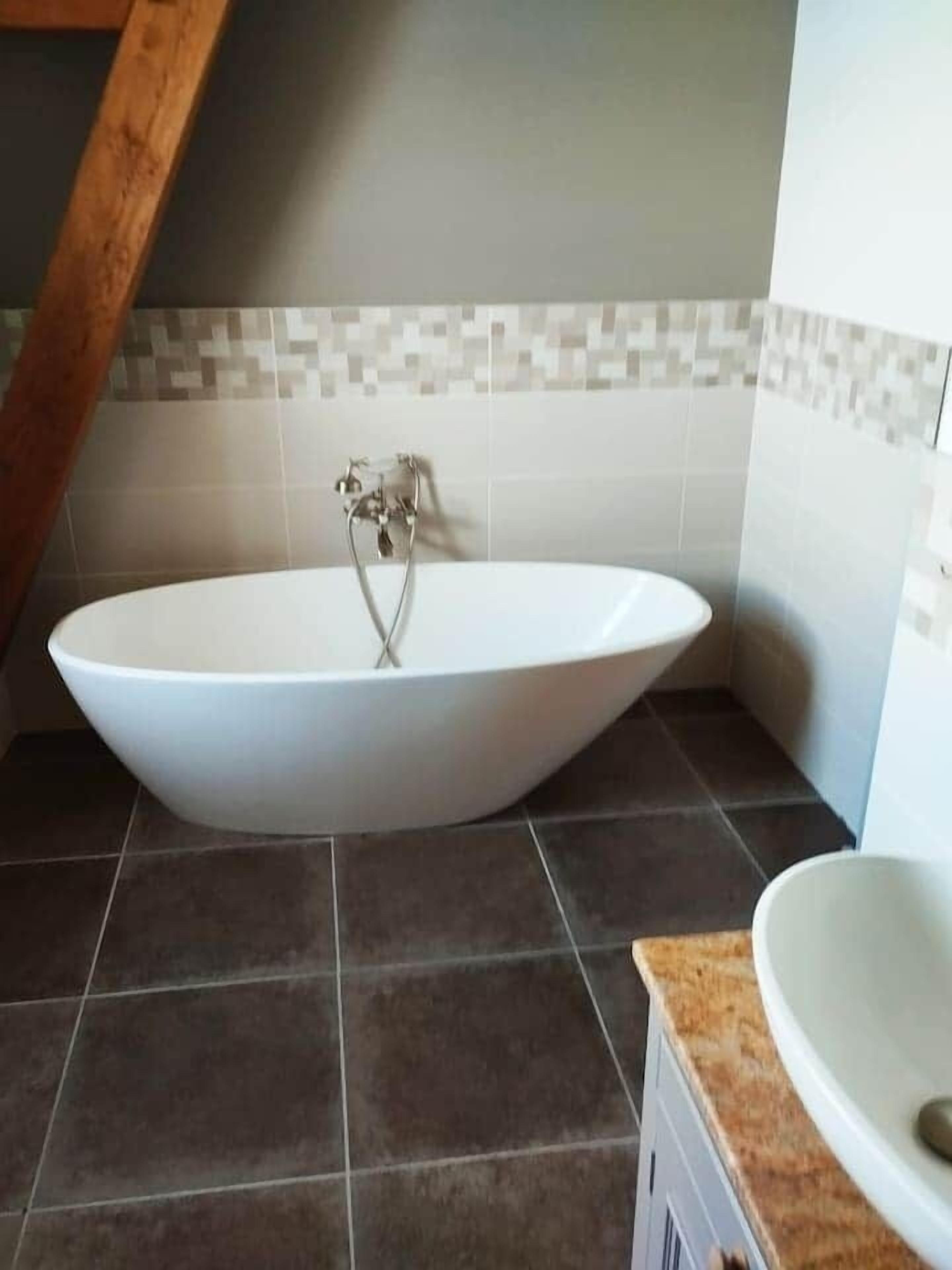 Un baño moderno con una bañera independiente, suelo de baldosas oscuras y un salpicadero de azulejos.