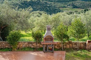 Mur de pedra amb un forn de pedra, envoltat d'oliveres i vegetació.