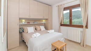 Een slaapkamer met een bed, nachtkastje, raam met gordijnen en een kledingkast.