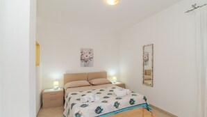 Un dormitorio con una cama, dos mesitas de noche con lámparas, un espejo y una obra de arte floral en la pared.
