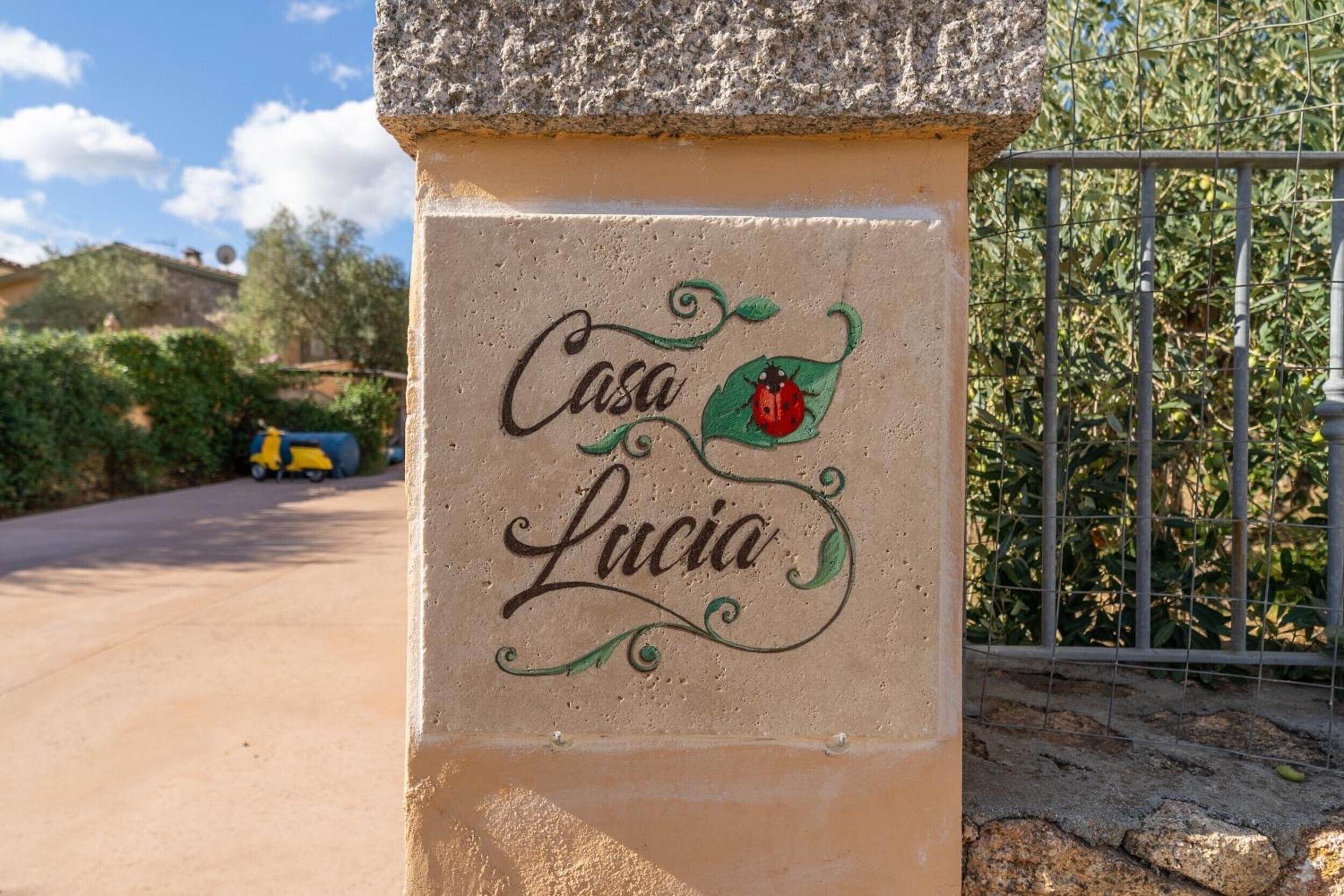 A stone pillar with 'Casa Lucia' written on it, surrounded by greenery and a fence.