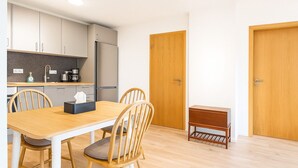 A modern kitchen with white cabinets, a wooden dining table, and chairs. There is a small wooden stool and a door with a handle. - Cosy First Floor Apt near Harbour & Cafes (Hafnarfjörður)