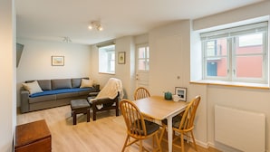 A compact living space with a sofa, a dining table, and chairs. There is a window with blinds, a radiator, and a ceiling light fixture. - Cosy First Floor Apt near Harbour & Cafes (Hafnarfjörður)