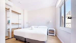 A modern bedroom with a large bed, a wardrobe, a small bedside table, and a window with a view. - Recently refurbished 3 bedroom apartment with terrace (Barcelona)