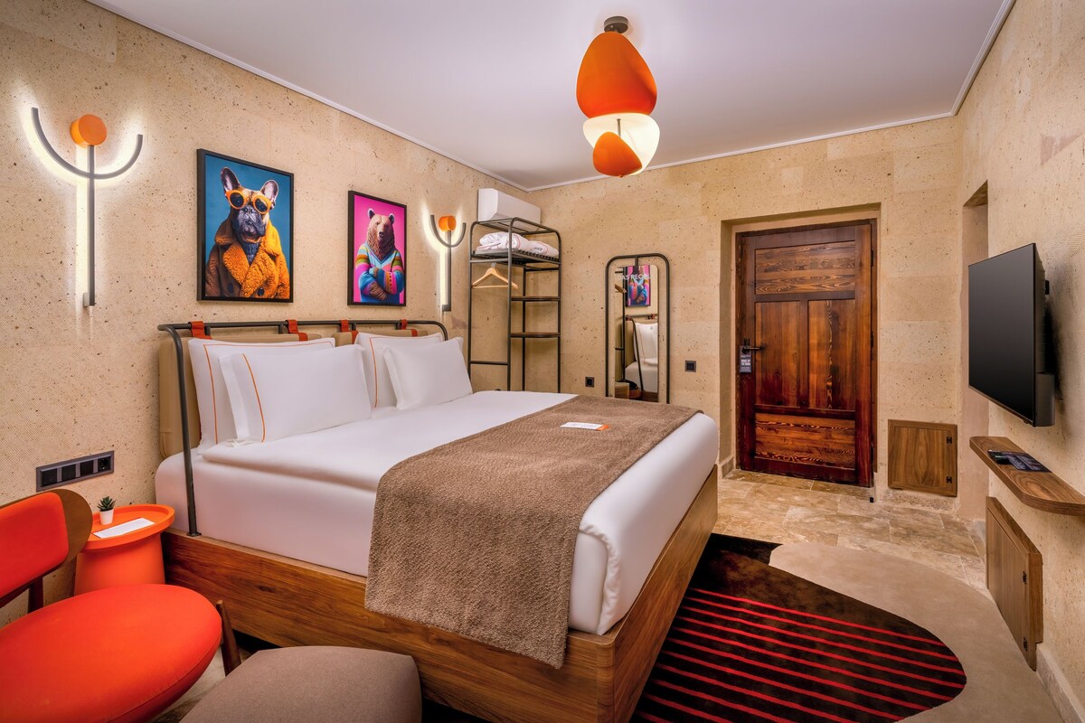 A hotel room with a bed, a TV, a wooden door, and a red chair.