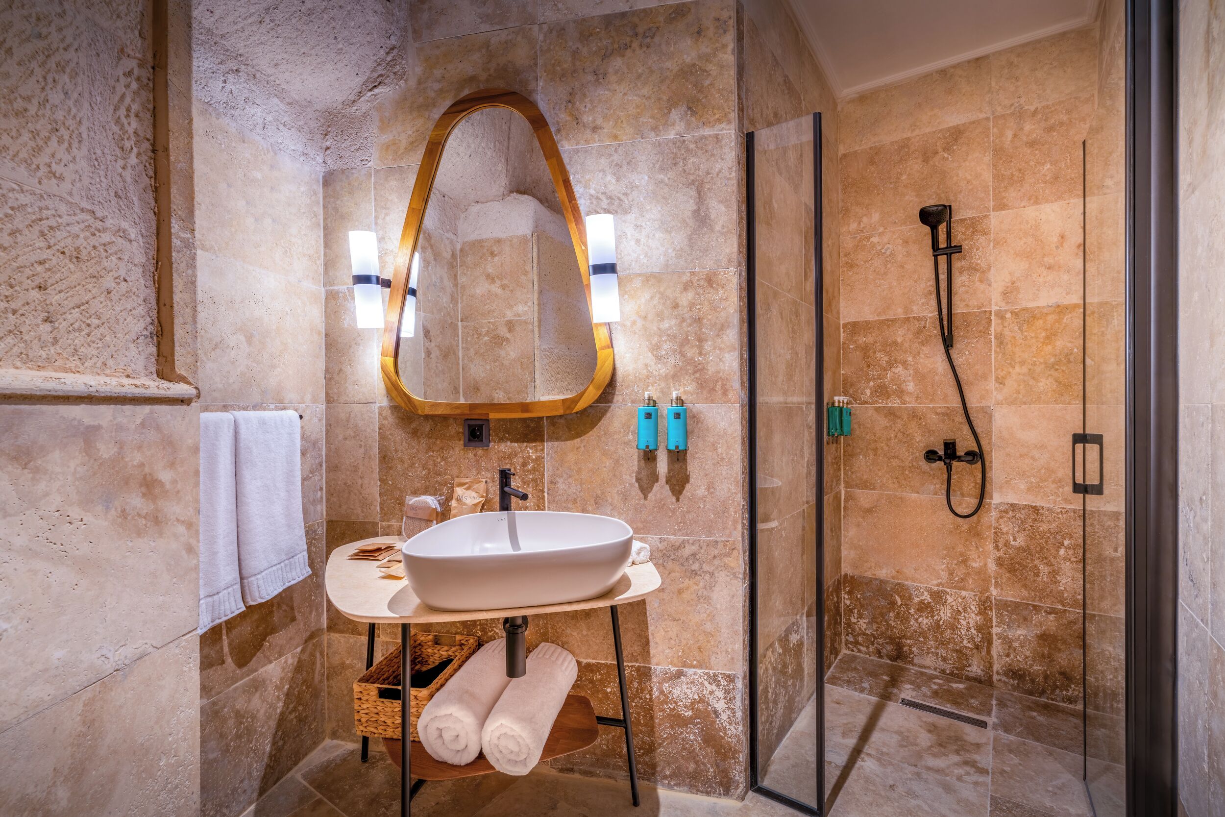 A modern bathroom with a large oval mirror, a white sink, a glass-enclosed shower, and a towel rack.