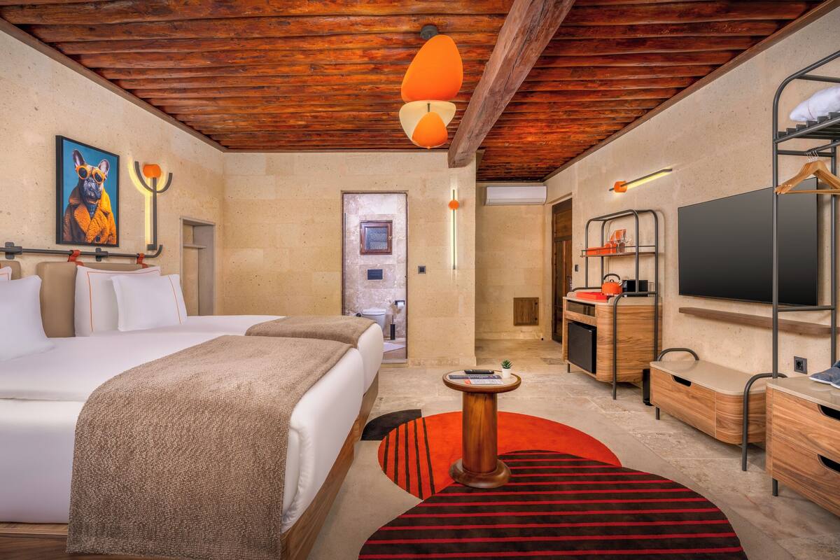Habitación de hotel con cama, escritorio, televisión y baño visible a través de una puerta abierta.