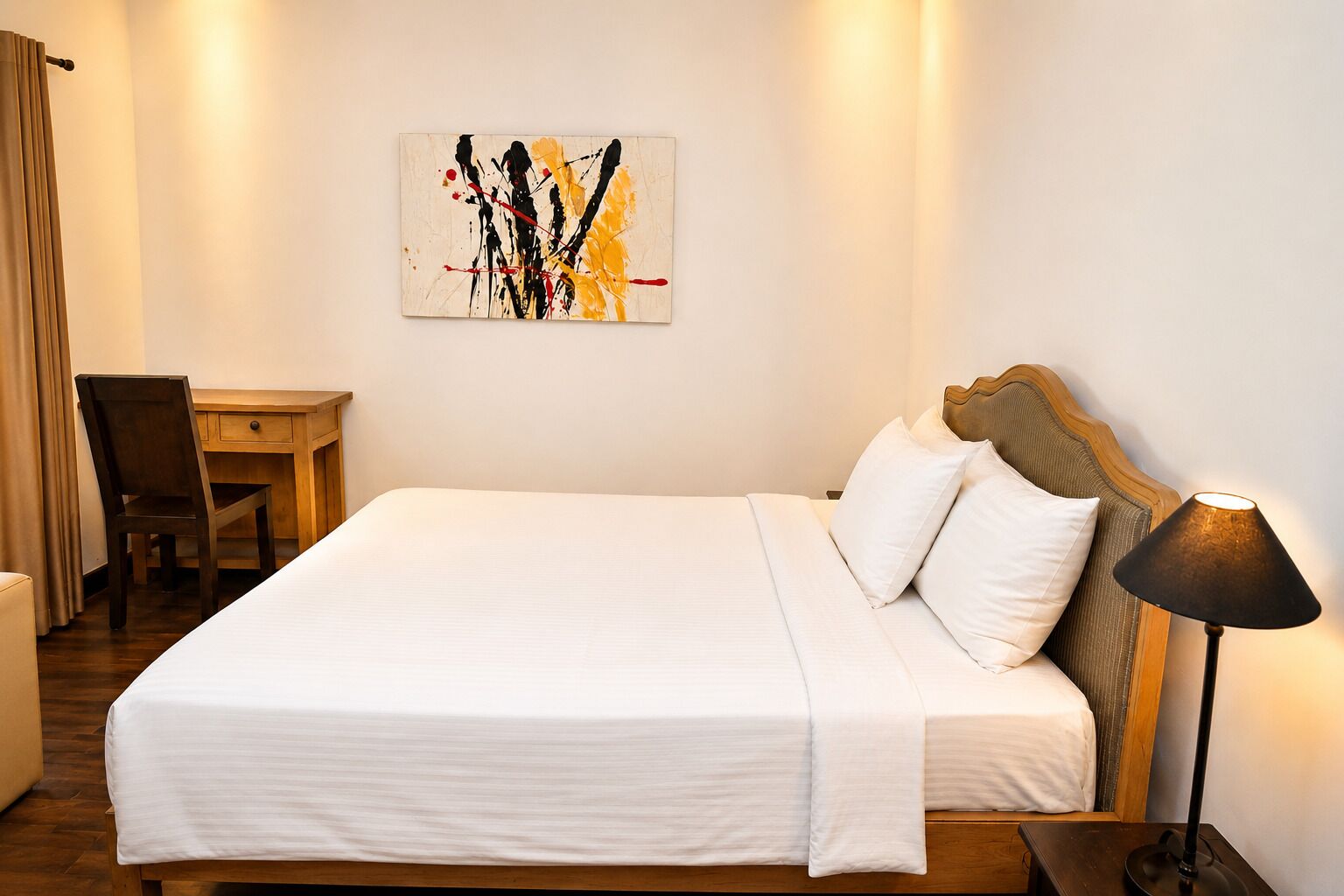 Habitación de hotel con una cama grande, un escritorio, una silla, una lámpara y un cuadro en la pared.