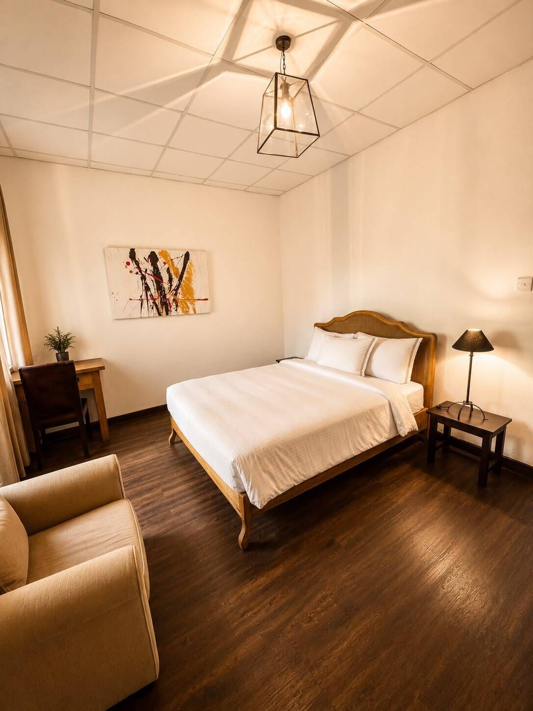 A bedroom with a wooden bed, a desk, a chair, a bedside table with a lamp, and a ceiling light fixture.