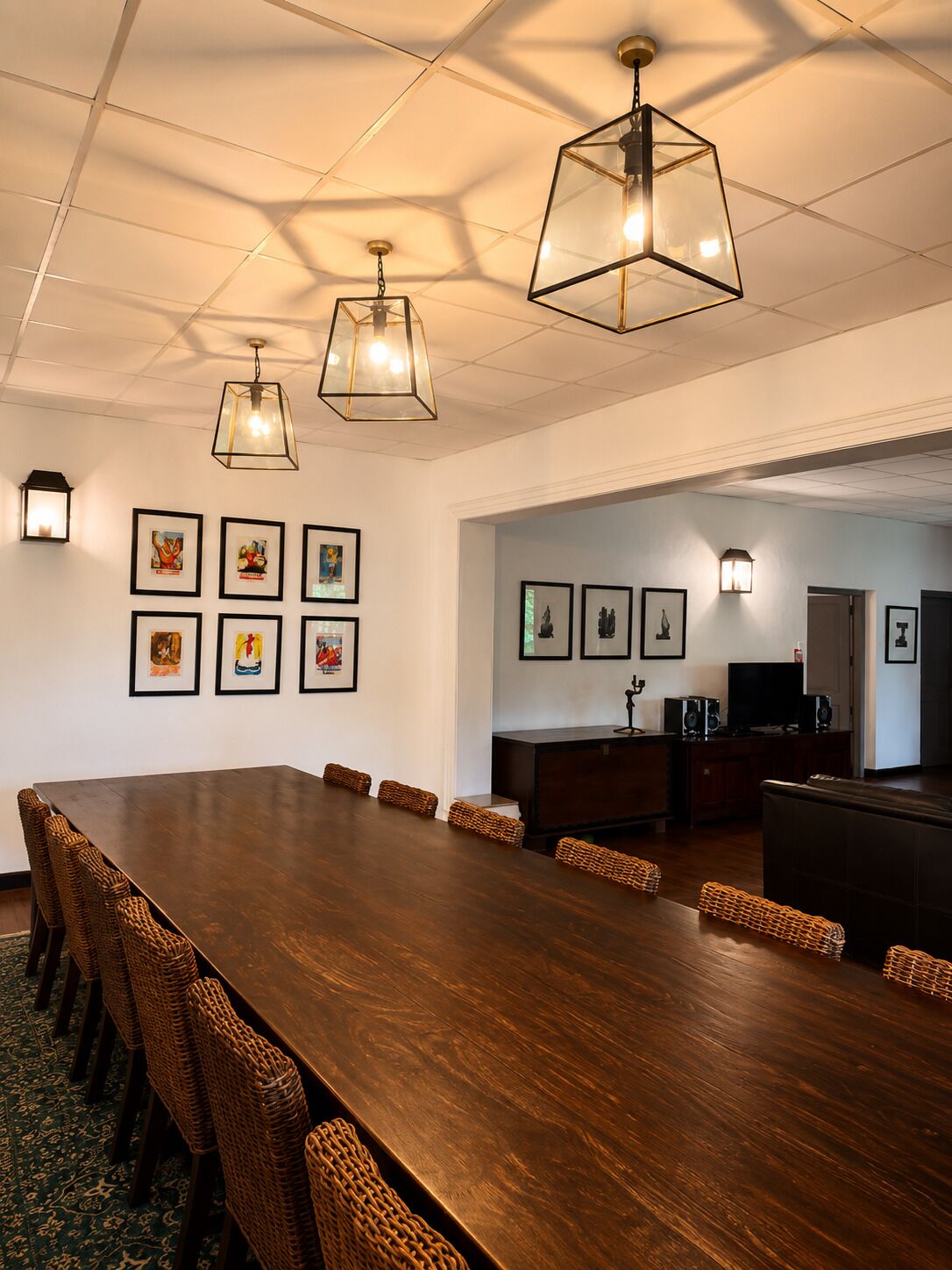 A conference room with a long table, wicker chairs, framed artwork on the walls, and pendant lighting.