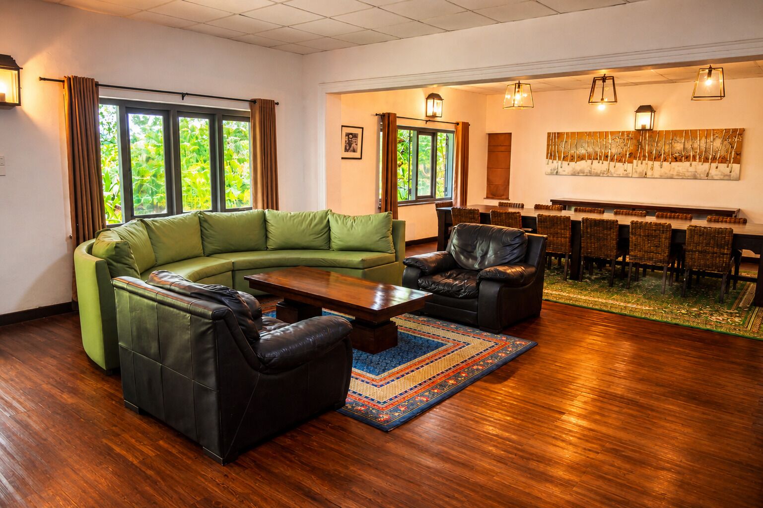A modern living room with a green sectional sofa, a black leather armchair, a wooden coffee table, and a dining area with wicker chairs and a long table.