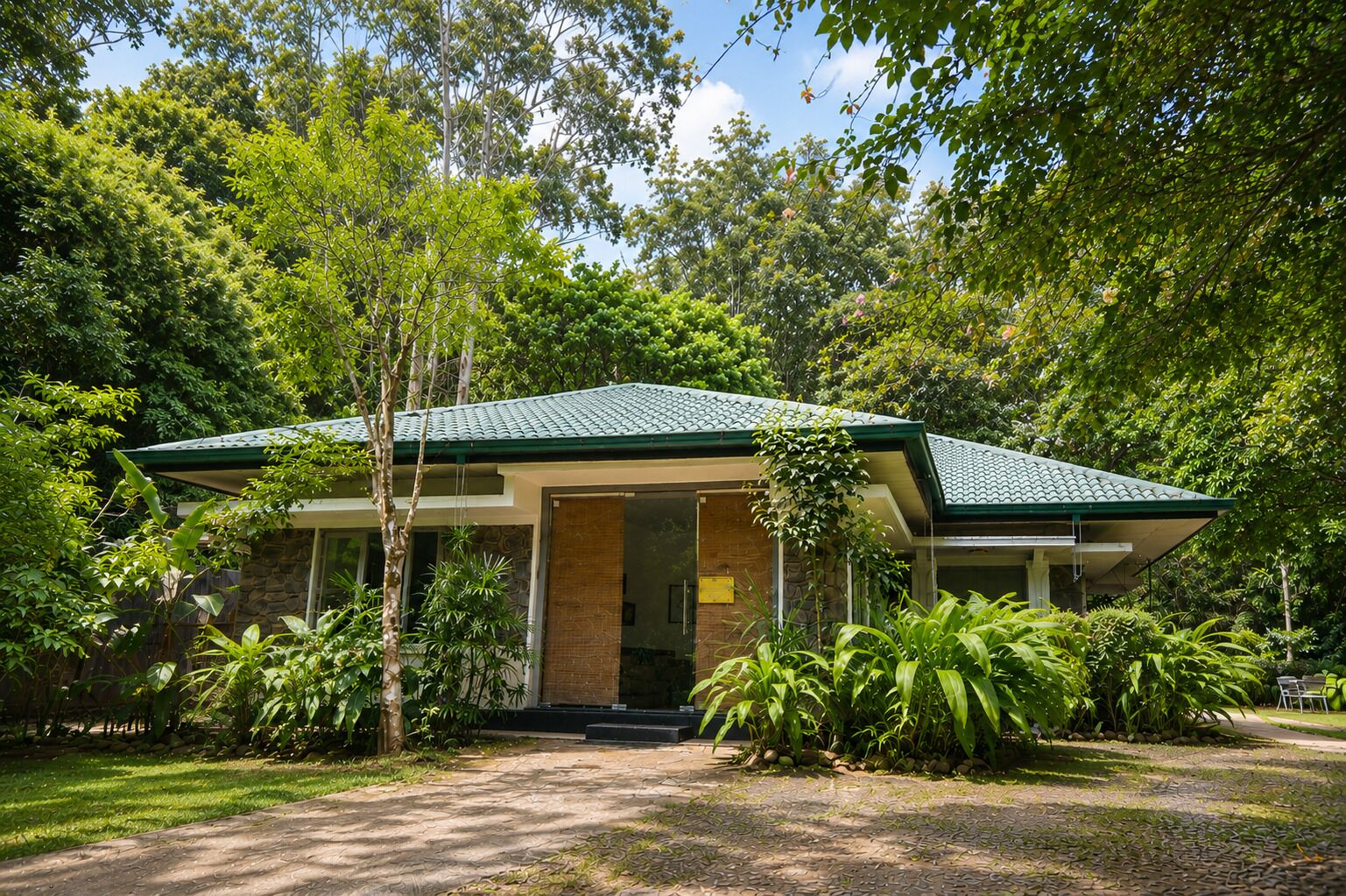 A single-story building with a green roof, surrounded by lush greenery and trees.