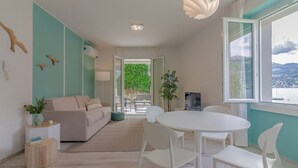 A modern living room with a sofa, a dining table with chairs, a TV, and a large window with a view.