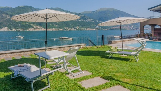 A poolside area with lounge chairs and umbrellas, overlooking a body of water and mountains.