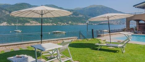 A poolside area with lounge chairs and umbrellas, overlooking a body of water and mountains.