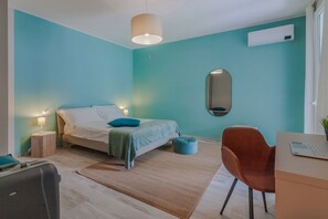 Un dormitorio con cama, lámparas de noche, escritorio, silla y maleta.