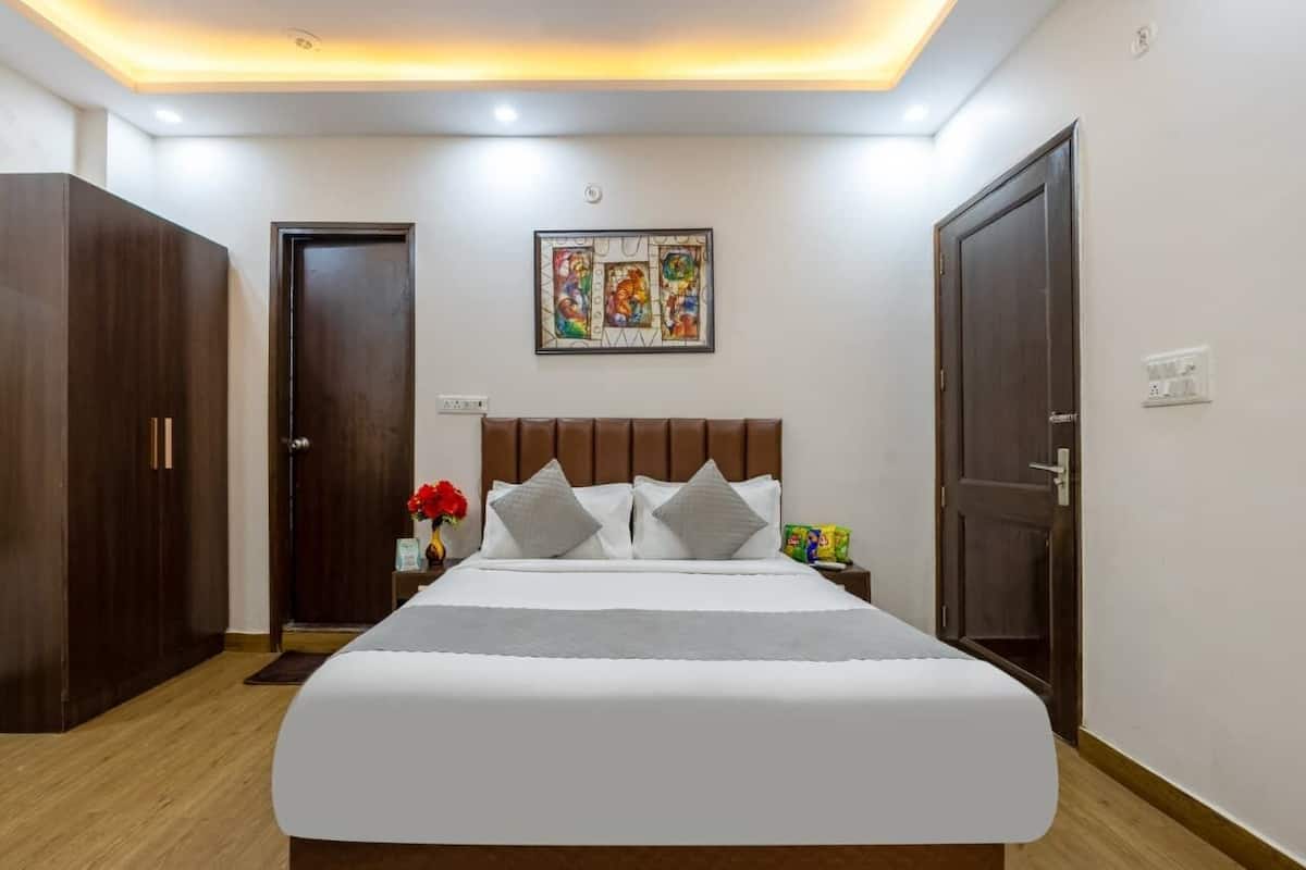Ein Hotelzimmer mit Bett, Nachttisch, Blumen in einer Vase, einer Tür und einem Wandbild.
