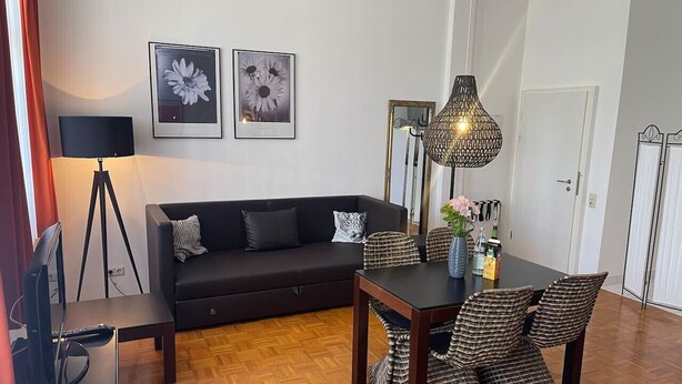 A living room with a sofa, a dining table with chairs, a lamp, and two framed pictures on the wall. - Bright Studio Apartment in Konstanz (Konstanz)