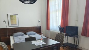 A hotel room with a bed, a desk with a laptop, a chair, a TV on a stand, and a window with curtains. - Bright Studio Apartment in Konstanz (Konstanz)