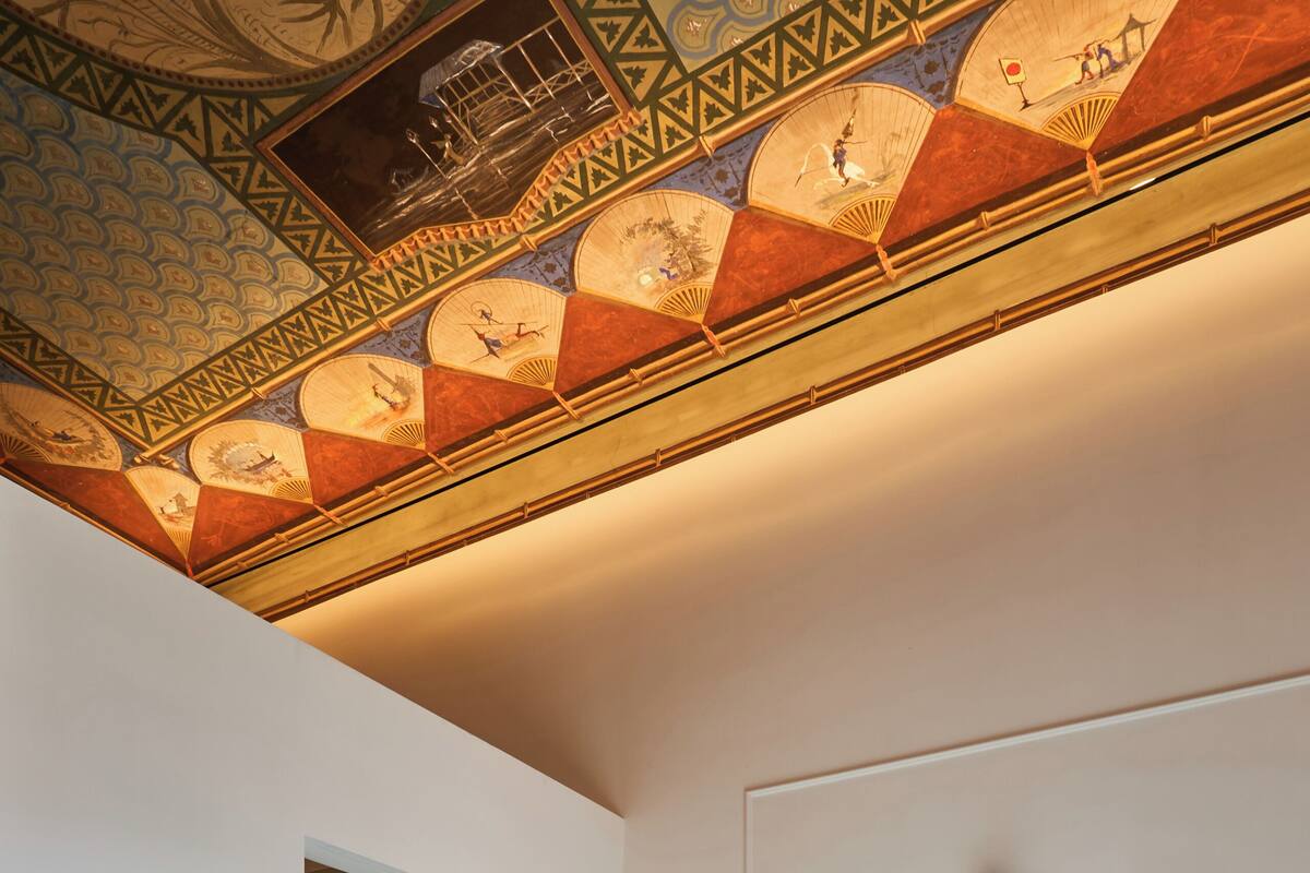 A hotel room with a bed, a door, a ceiling with a decorative pattern, and a wall-mounted light fixture.