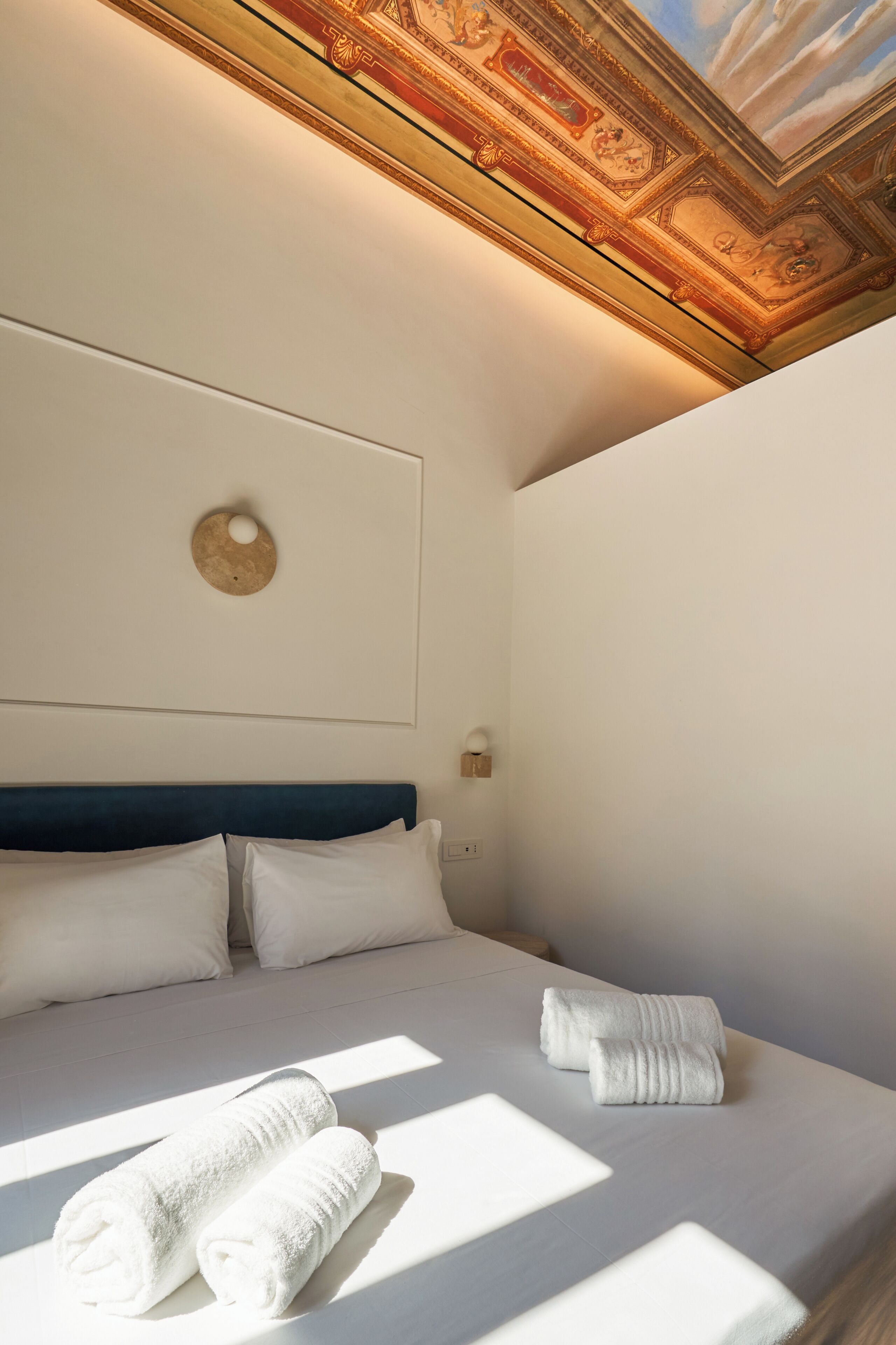Een hotelkamer met een bed, kussens, een wandklok en een plafond met decoratieve details.