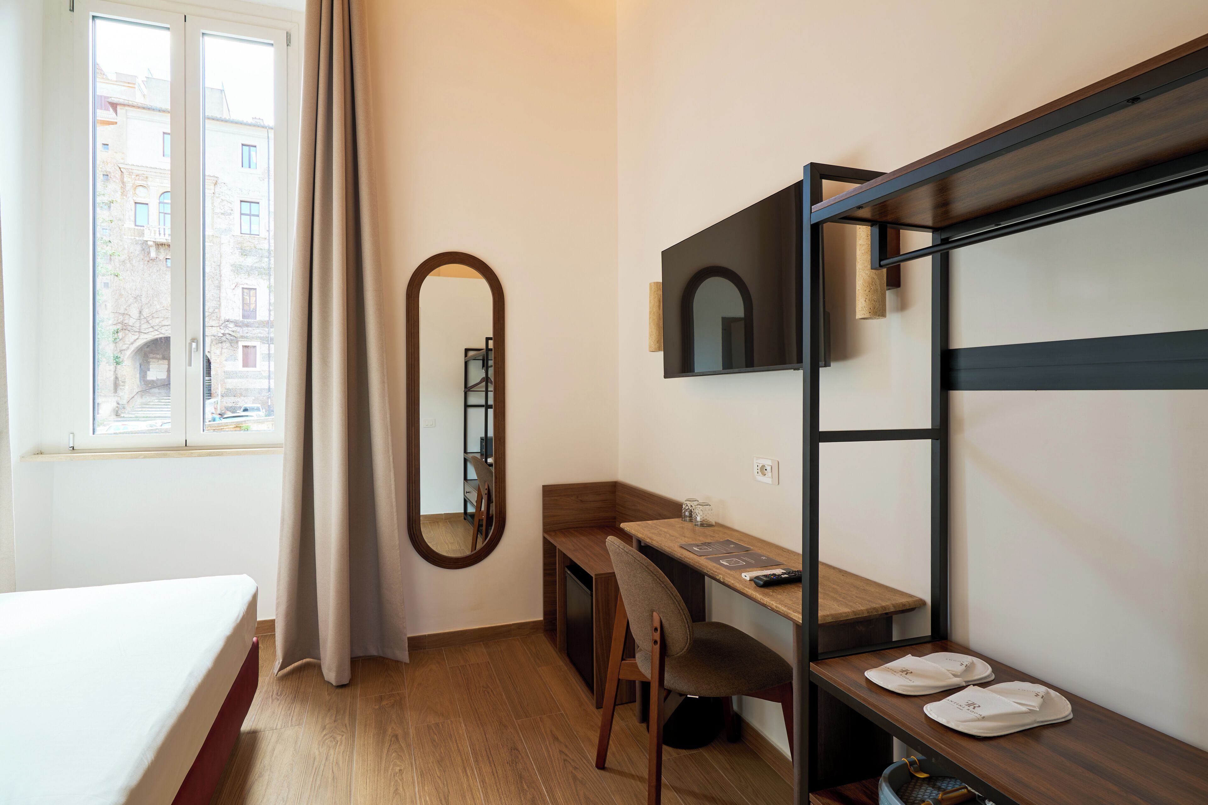 A hotel room with a bed, a desk, a chair, a mirror, and a window with curtains.
