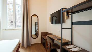 A hotel room with a bed, a desk, a chair, a mirror, and a window with curtains.
