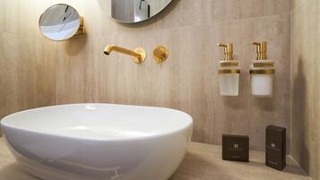 Un baño con un lavabo grande blanco, accesorios dorados, un espejo redondo y dos dispensadores de jabón.