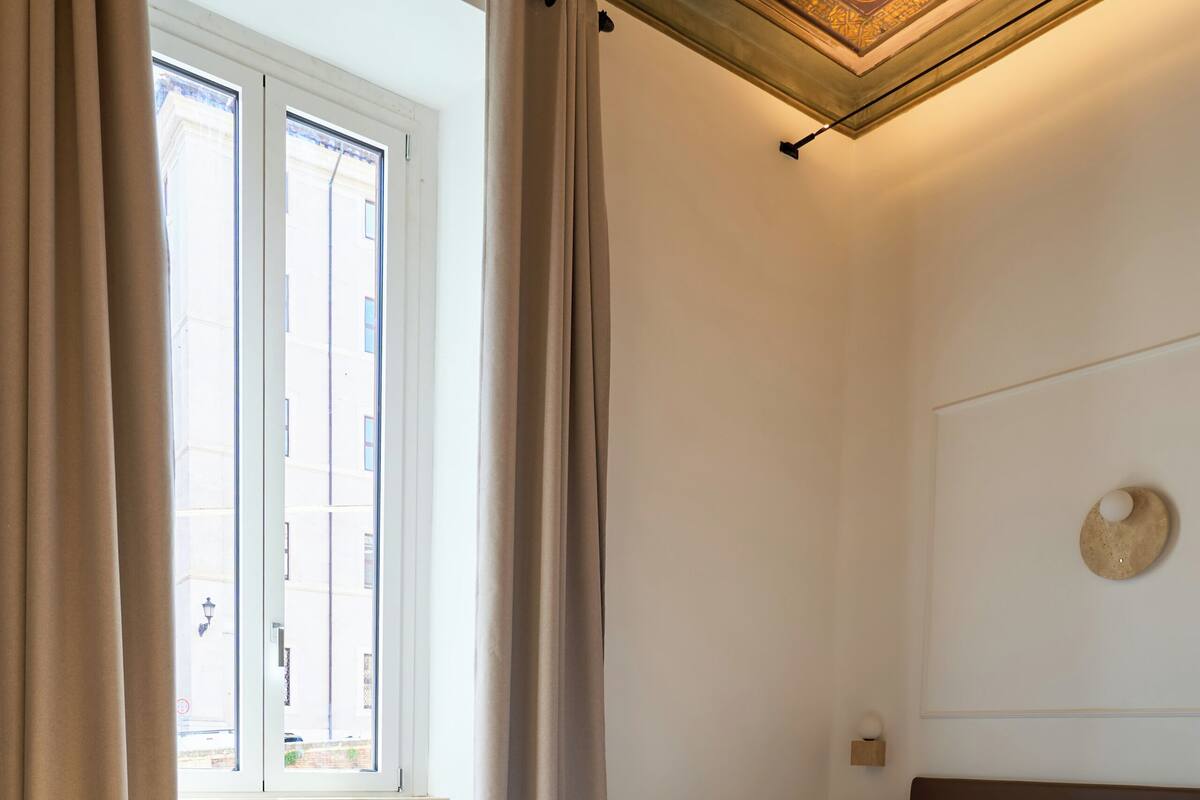 A bedroom with a bed, curtains, a window, and a ceiling with a decorative design.