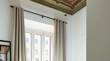 Una habitación de hotel con cama, escritorio, silla, ventana con cortinas y techo con diseño decorativo.