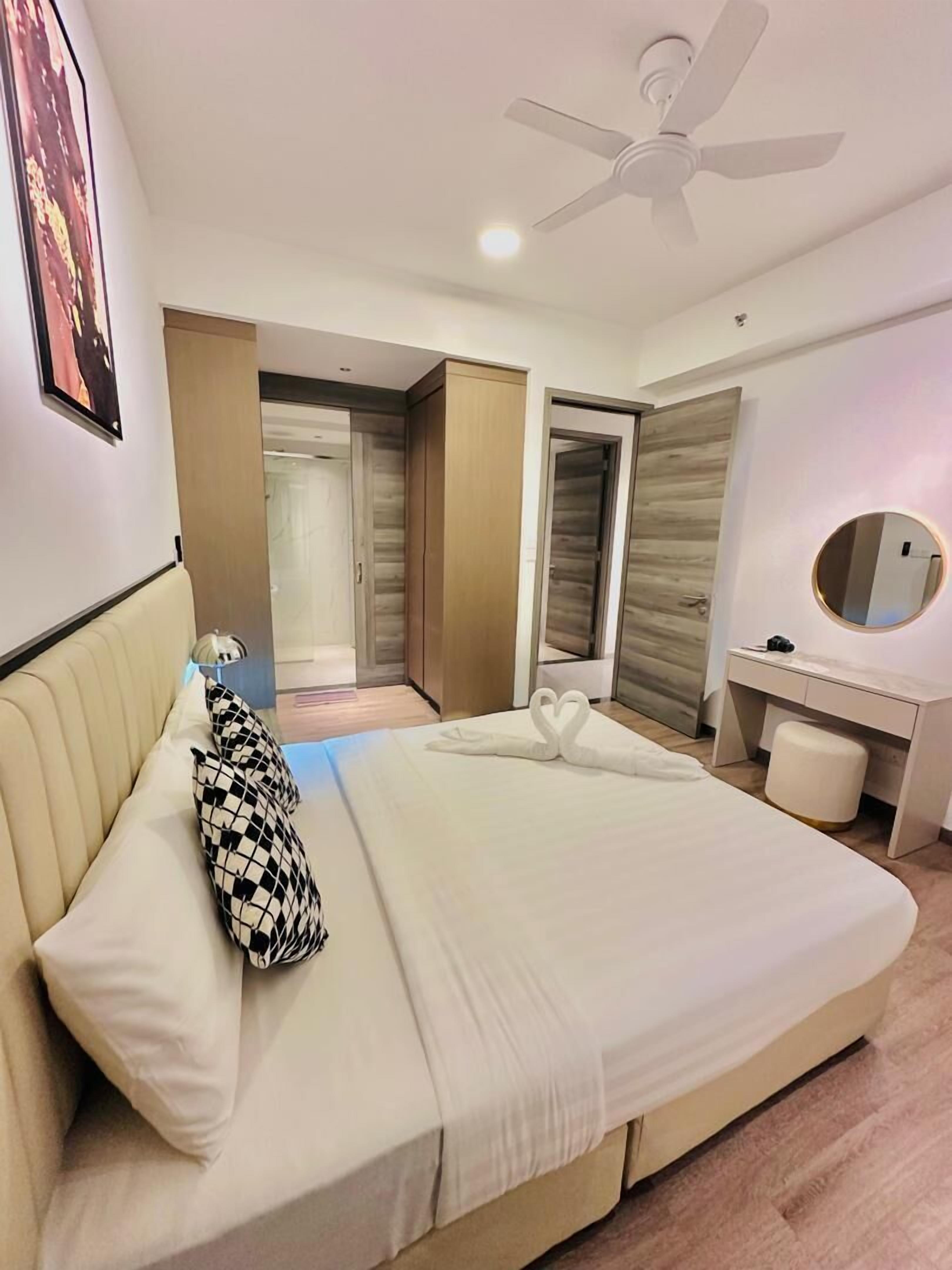 A modern hotel room with a large bed, a ceiling fan, a desk with a mirror, and a wardrobe.