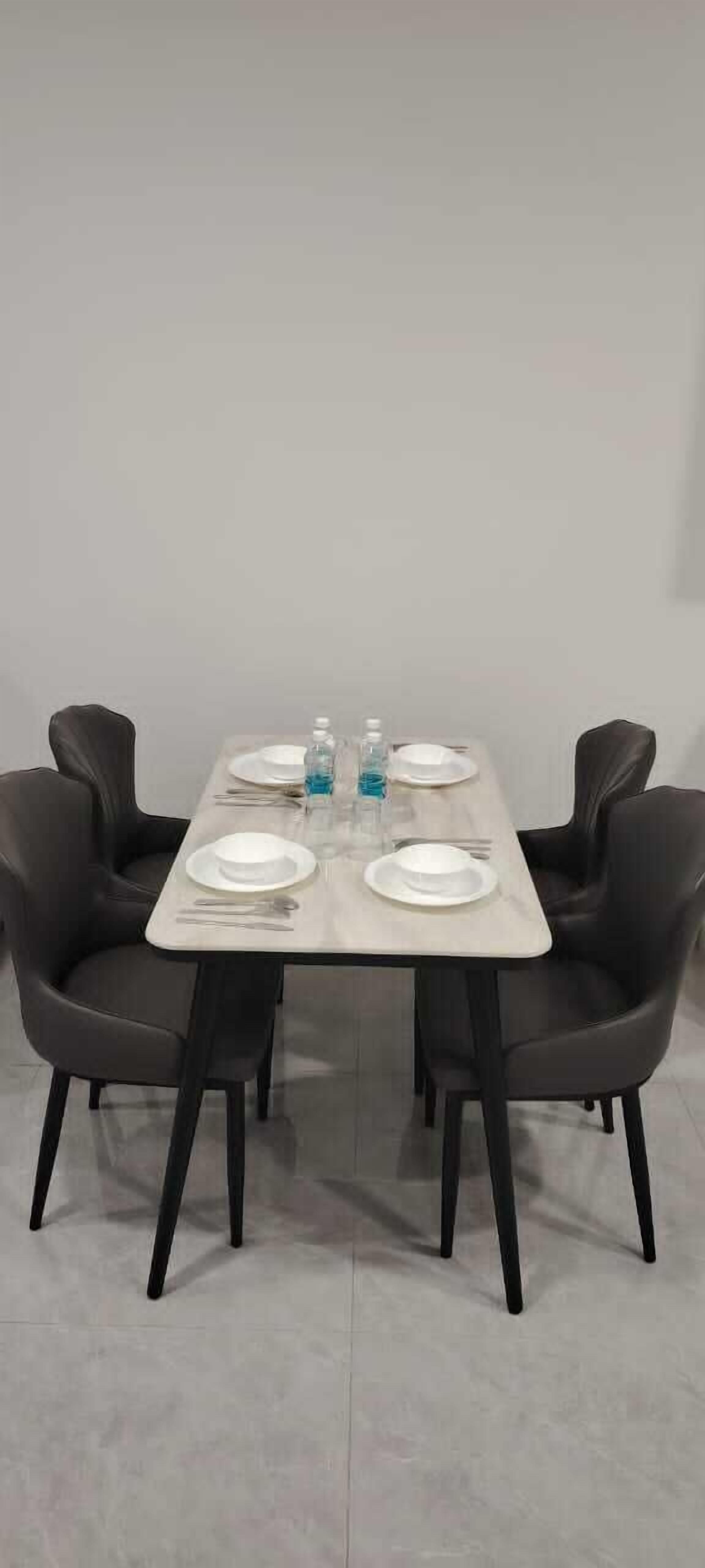 A dining table with four chairs, set with plates, cutlery, and a bottle of water.