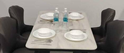 A dining table with four chairs, set with plates, cutlery, and a bottle of water.